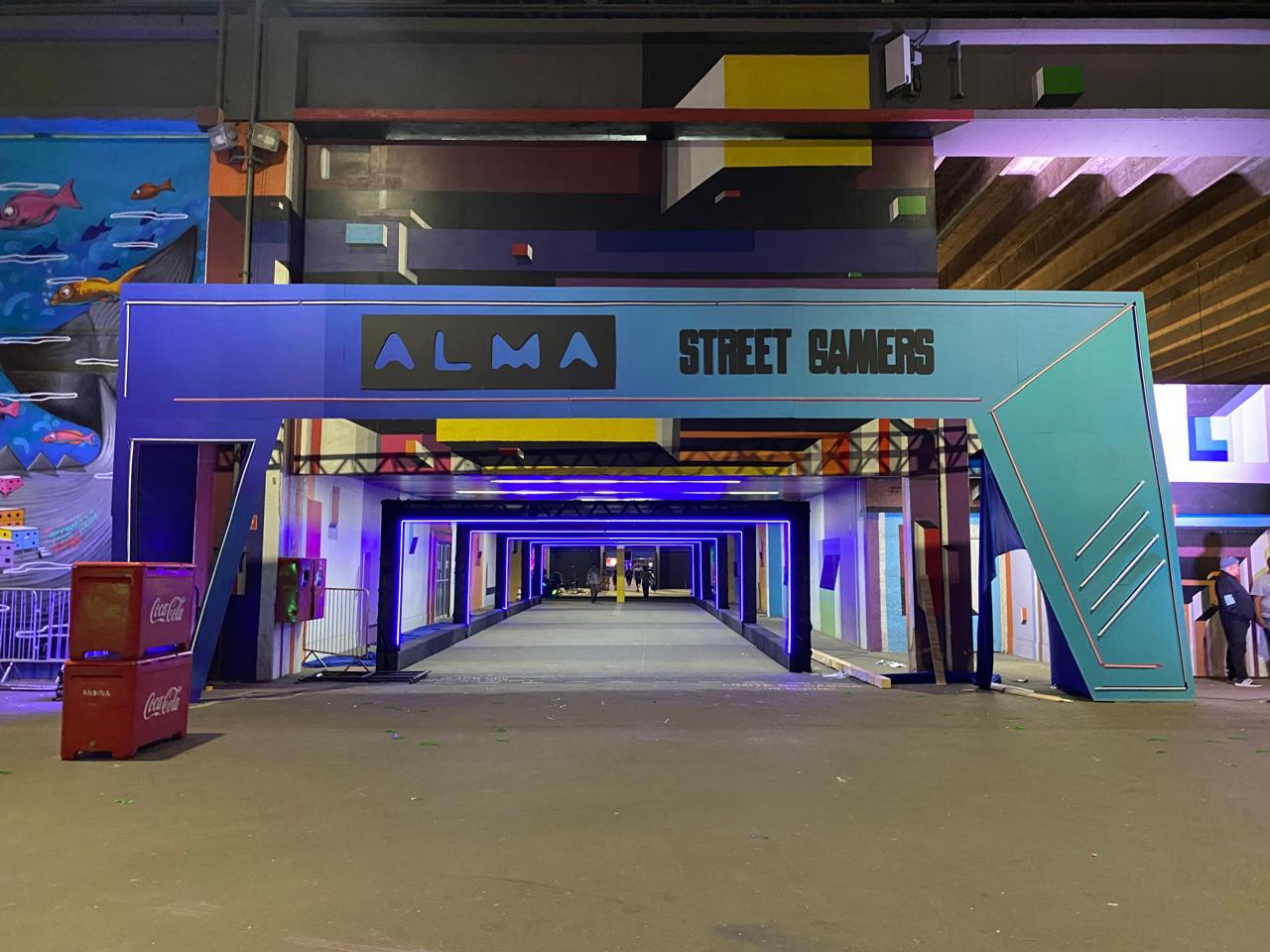 Pórtico cenográfico iluminado na entrada do ALMA Street Gamers